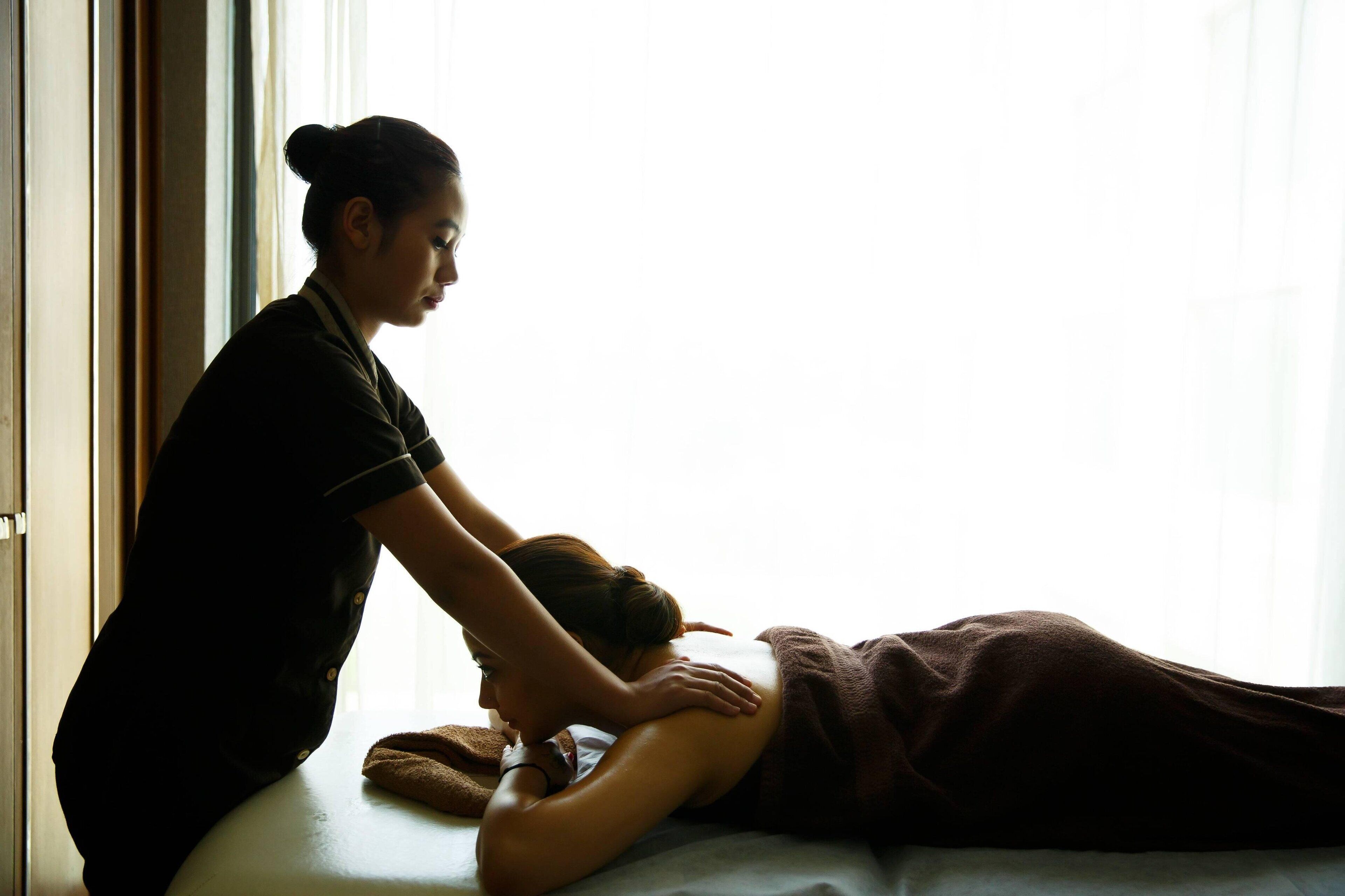 A massage therapy session in a room with a bed and a window.