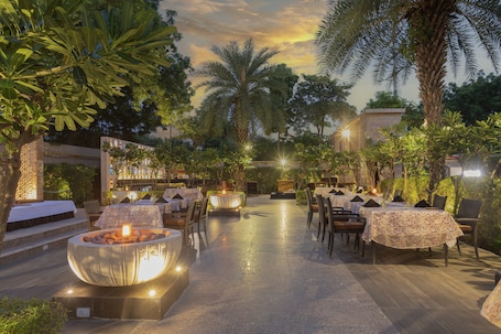 An outdoor dining area with tables and chairs, surrounded by lush greenery and palm trees.