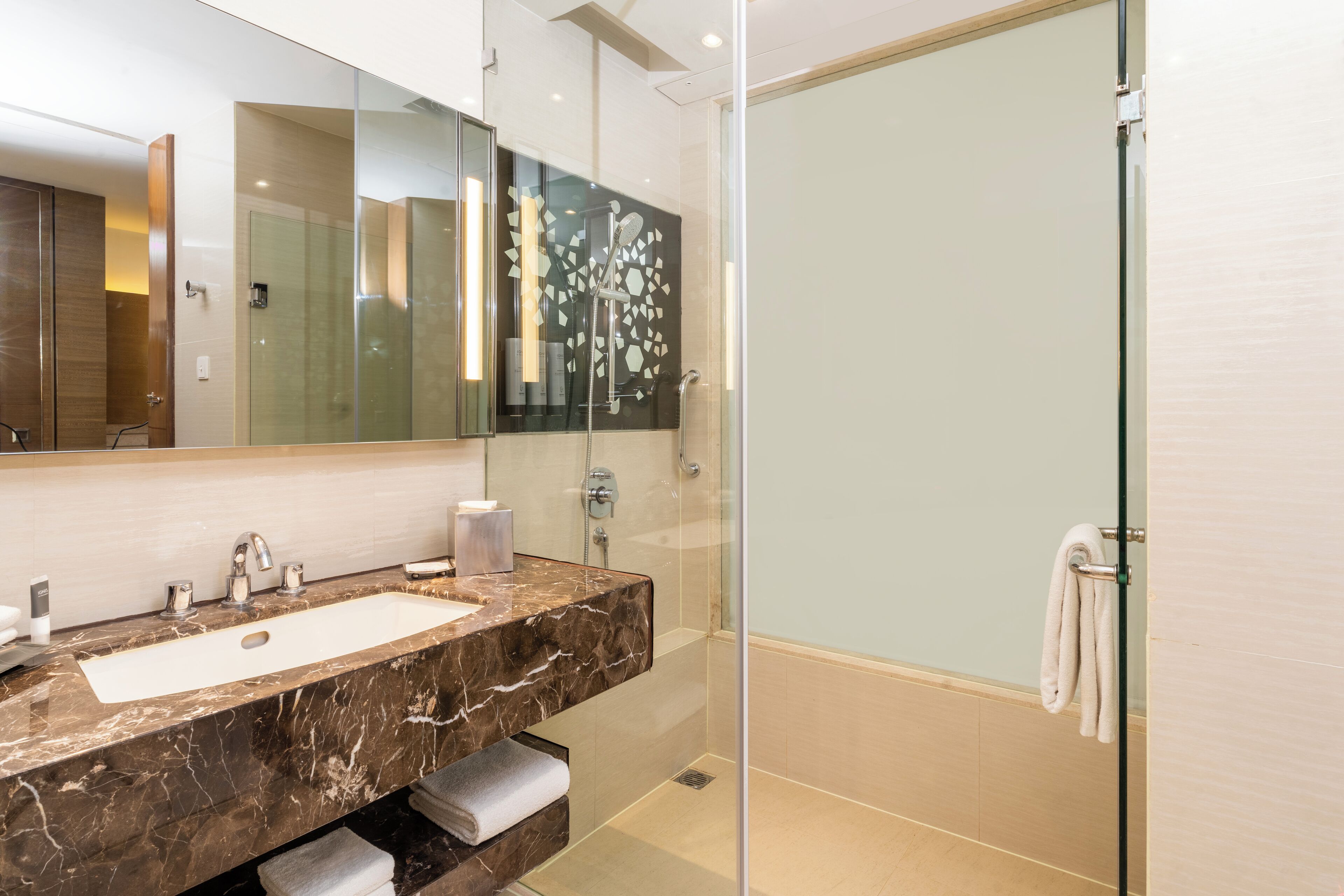 Un baño moderno con lavamanos de mármol, cabina de ducha de vidrio y un espejo grande.