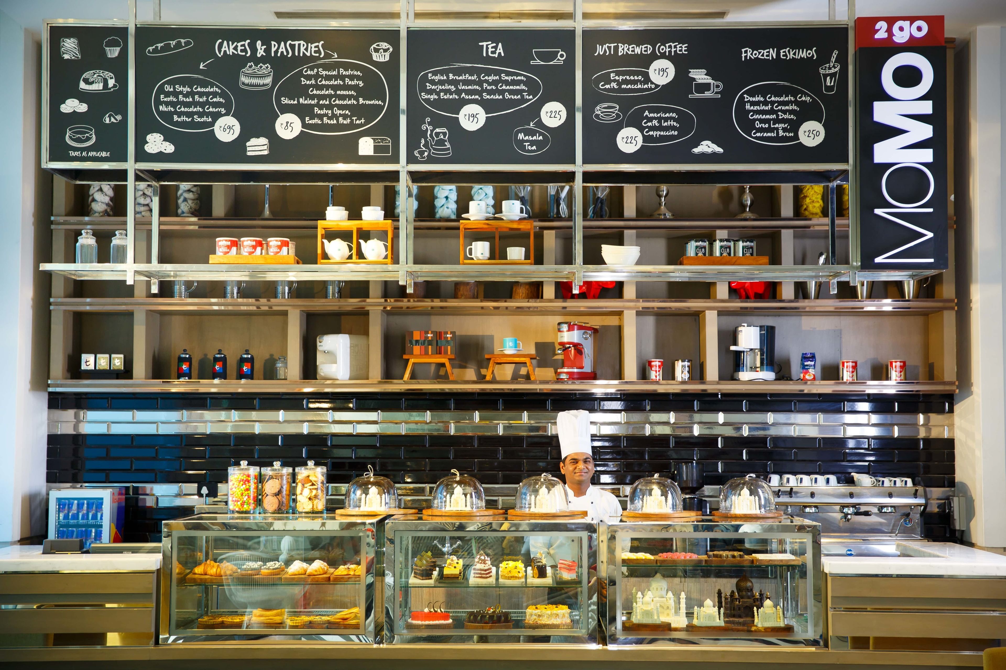 A cafe with a chalkboard menu listing cakes, pastries, tea, and coffee.