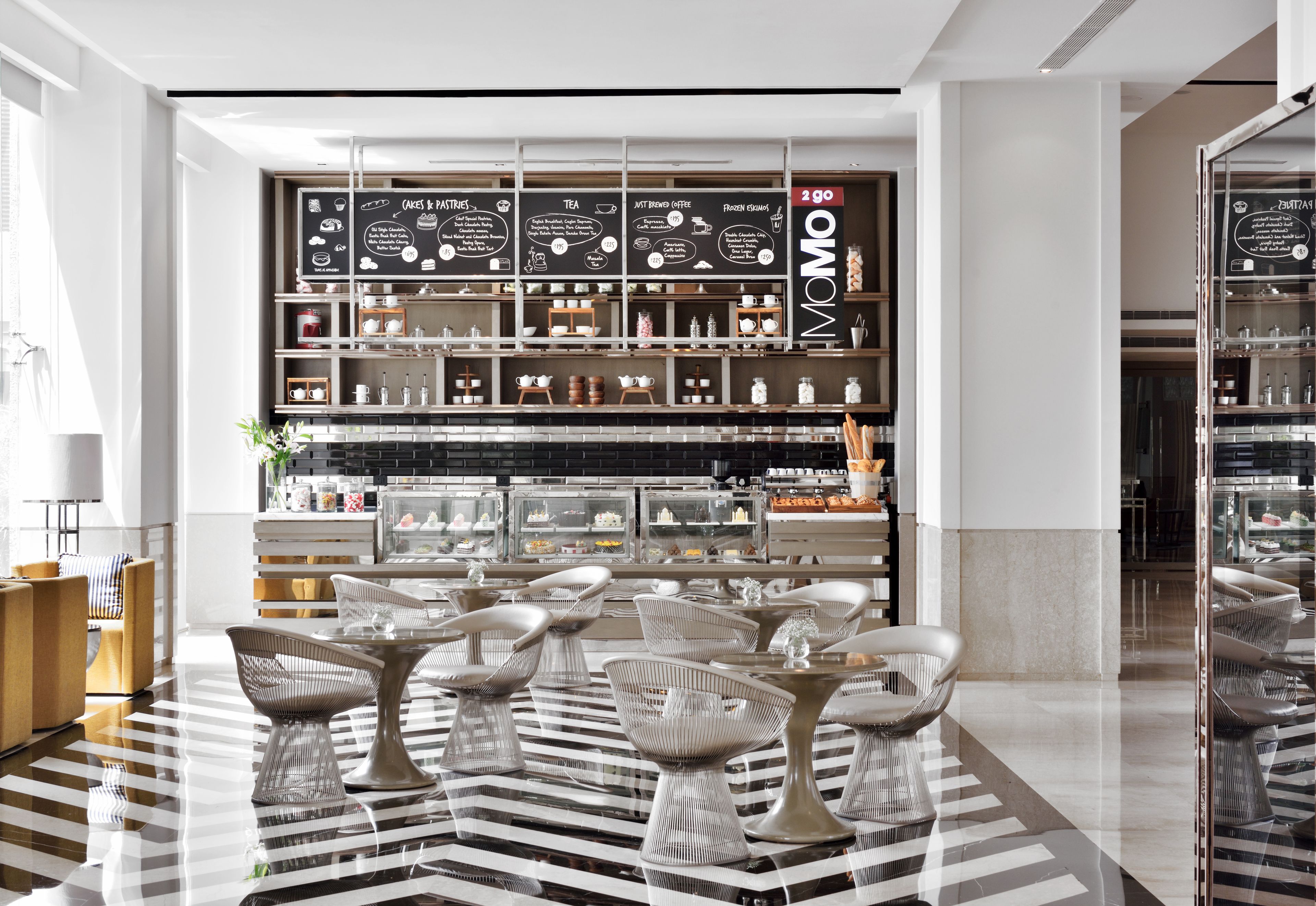 A modern cafe with a blackboard menu, white chairs, and a glass display case.