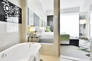 A modern hotel room with a large bathtub, a bed with a green blanket, and a mirror reflecting the room. - Courtyard by Marriott Agra (Agra)