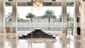 A spacious lobby with a reflective floor, a central water feature, and a view of palm trees and greenery outside. - Courtyard by Marriott Agra (Agra)