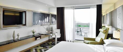 Habitación de hotel con una cama grande, televisor montado en la pared, escritorio con silla y vistas al exterior a través de un ventanal.