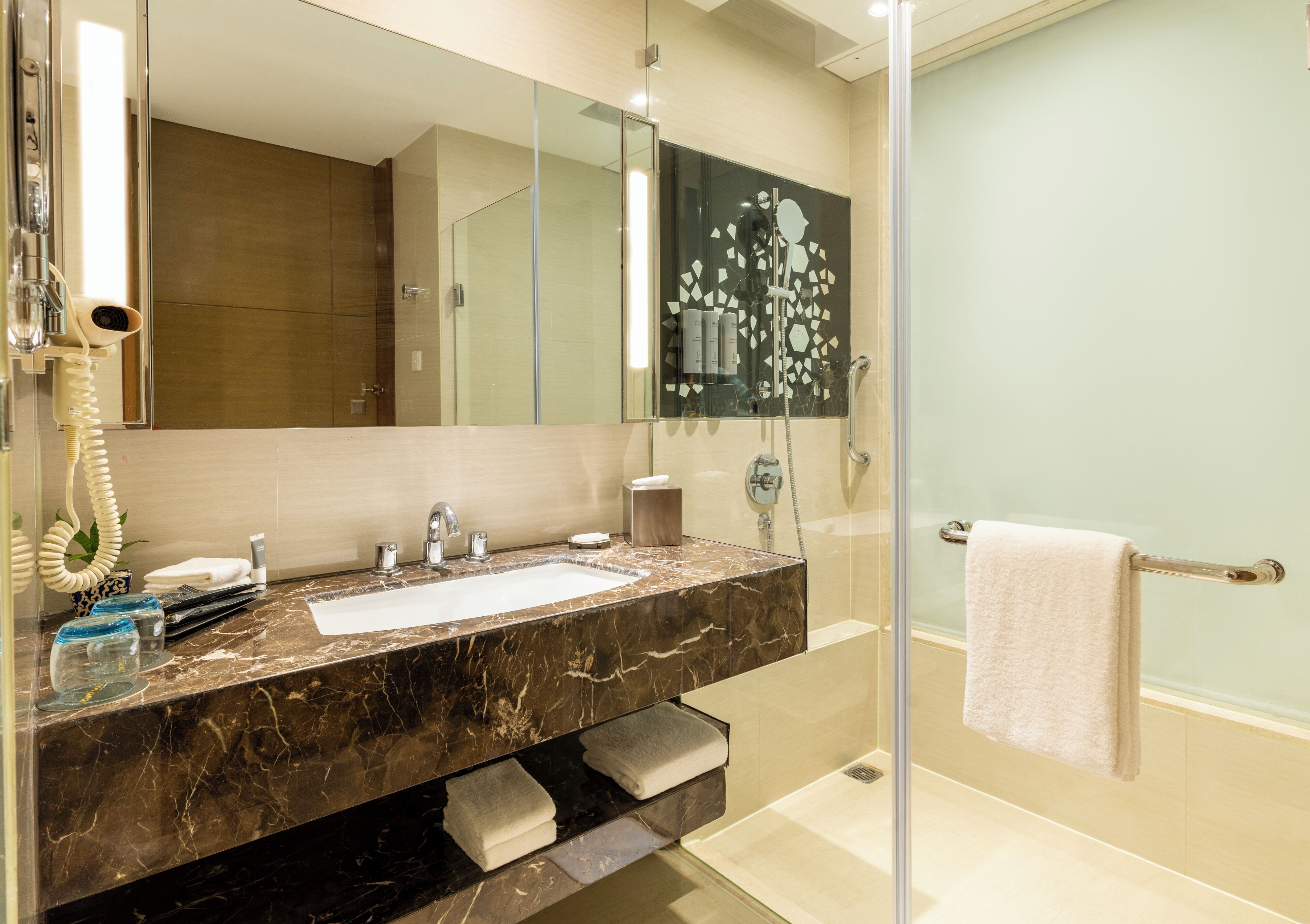 A modern bathroom with a marble sink, a large mirror, a glass shower enclosure, and a towel rack.
