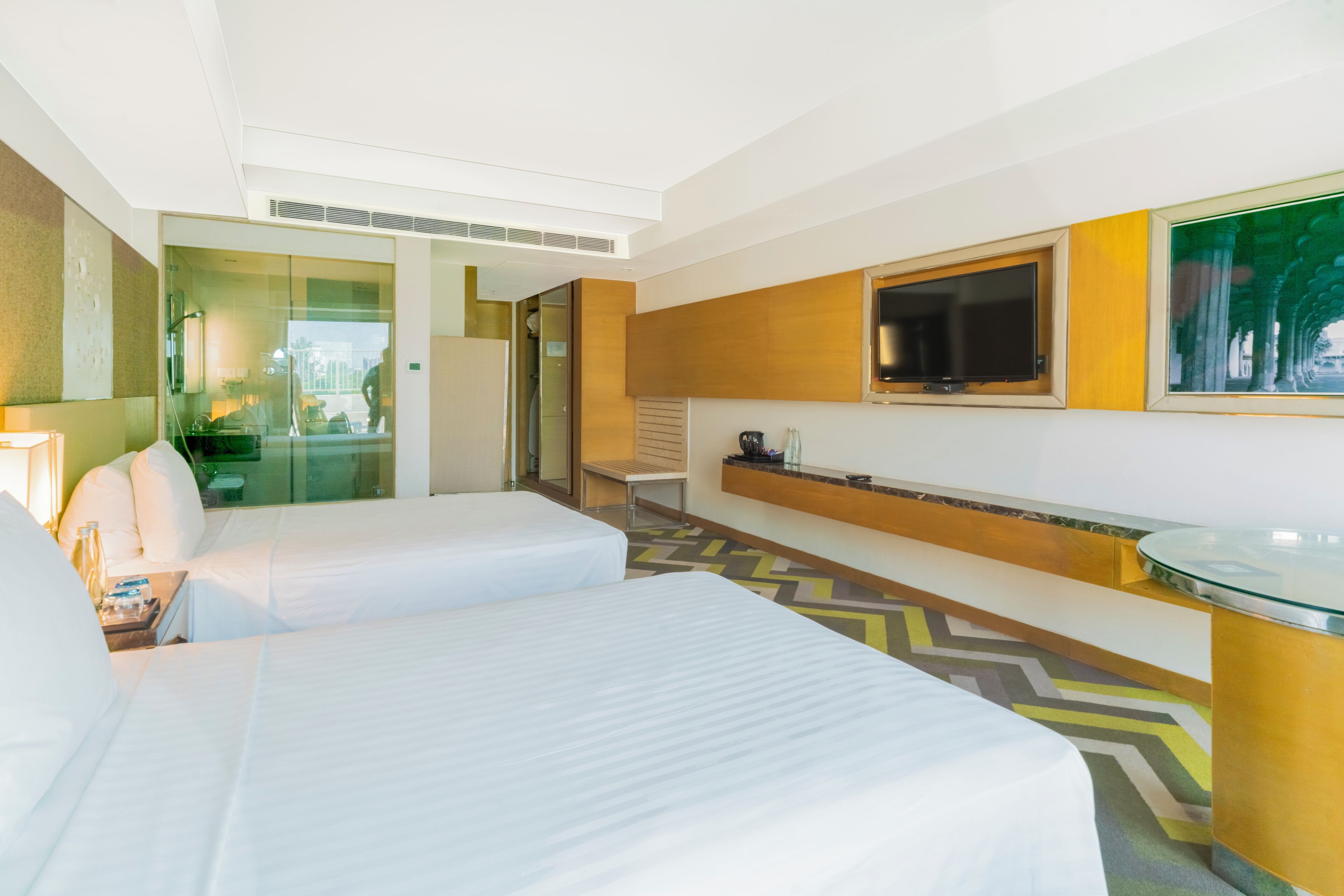 Habitación de hotel con dos camas, televisión, una mesa de vidrio y vista a la ciudad.