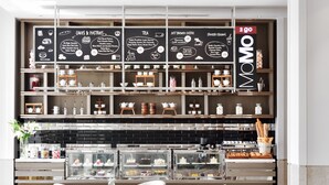 Un café moderno con una pizarra de menú, sillas de mimbre y una vitrina de vidrio.