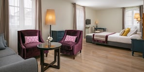 Habitación de hotel con dos sillones, una cama, un escritorio con ordenador y una mesita con lámpara.