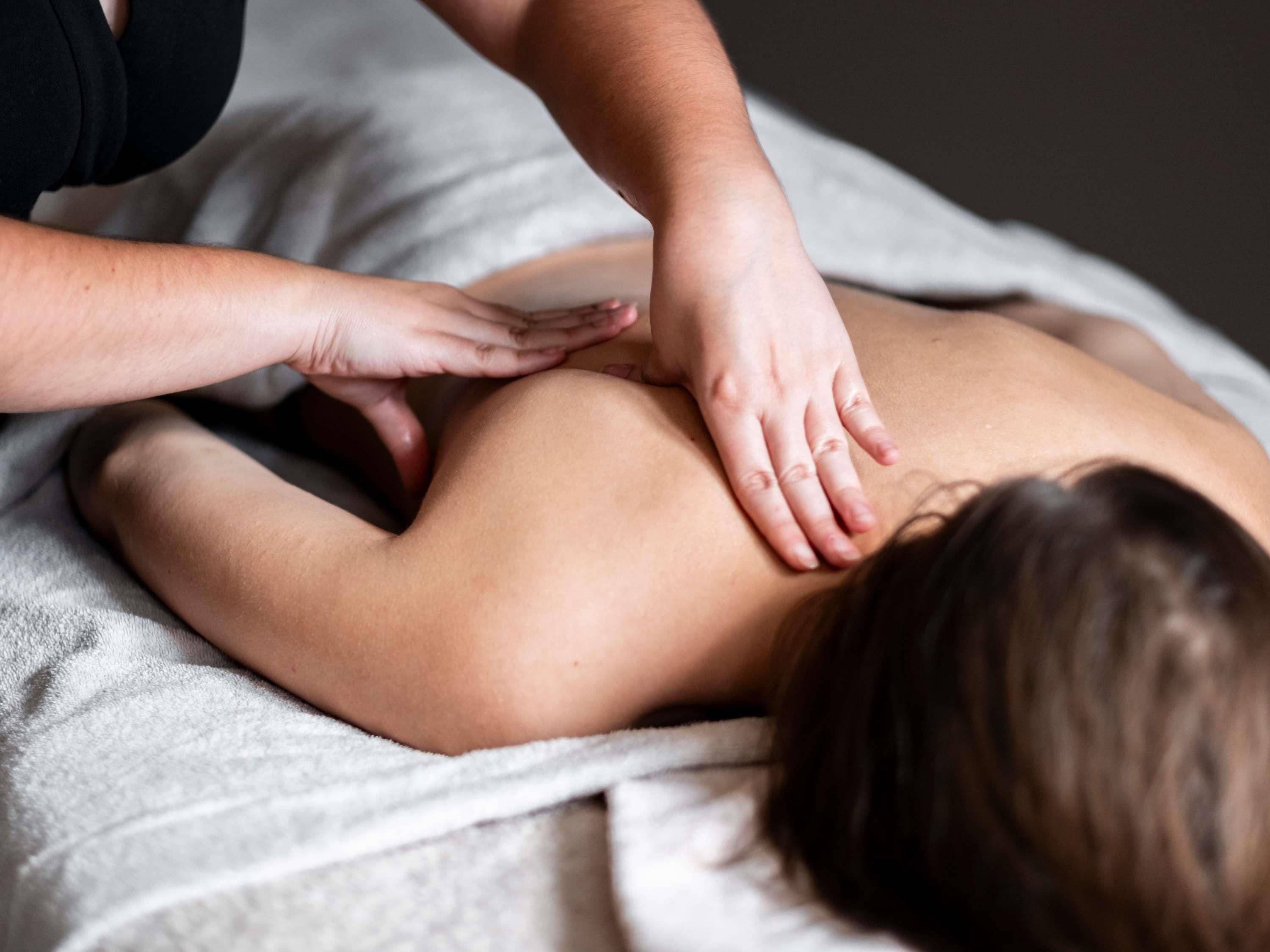 A person receiving a back massage on a bed with a white blanket.