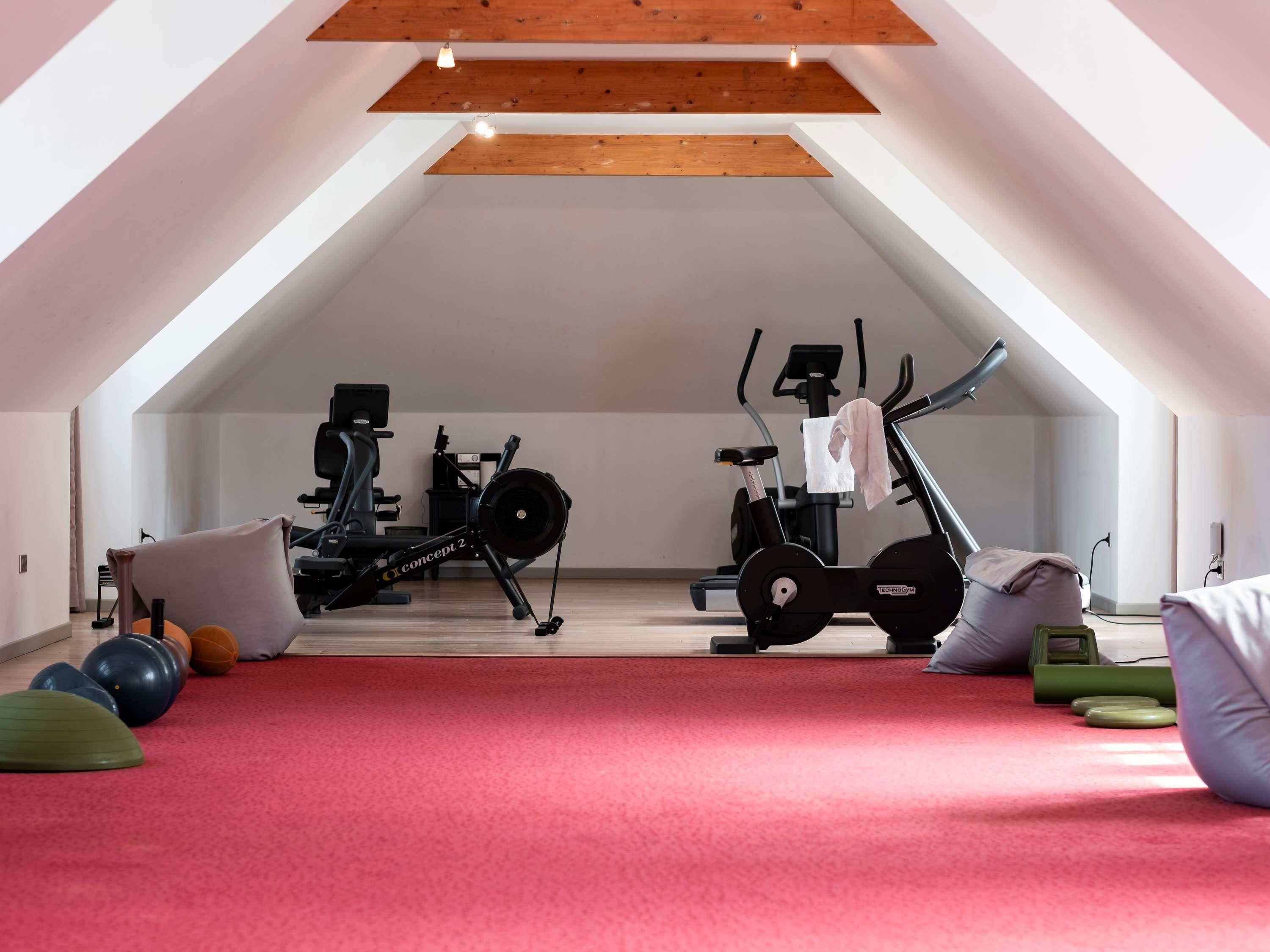 A spacious attic room with a sloped ceiling, exercise equipment, and a red carpet.
