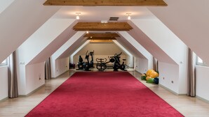 A spacious attic room with a red carpet, exercise equipment, and a wooden ceiling.