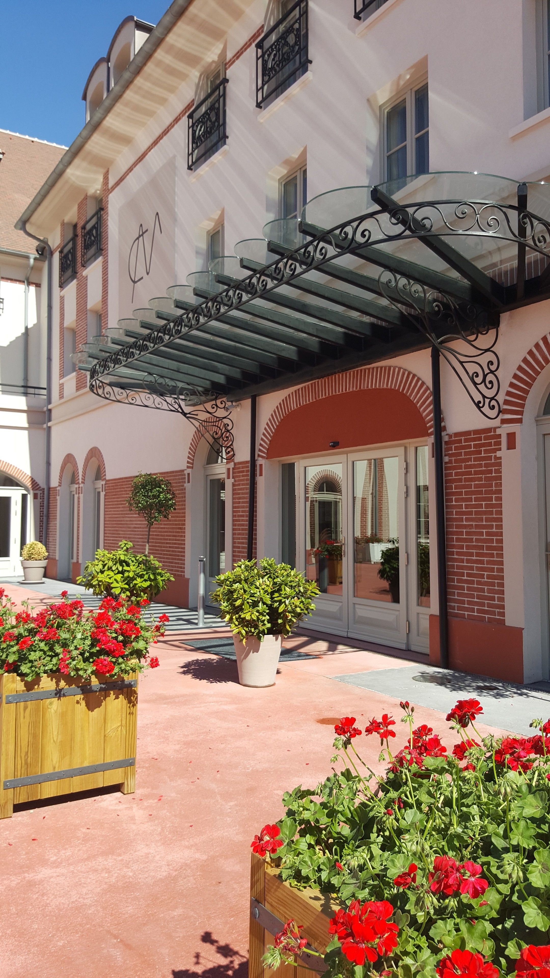 L’entrée d’un hôtel, avec un passage couvert, des plantes en pot et des fleurs rouges.