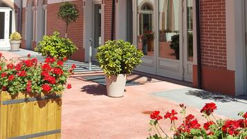 L’entrée d’un hôtel, avec un passage couvert, des plantes en pot et des fleurs rouges.