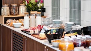 A buffet setup with various food items, including cheeses, meats, and condiments, arranged on a counter with a tiled backsplash.