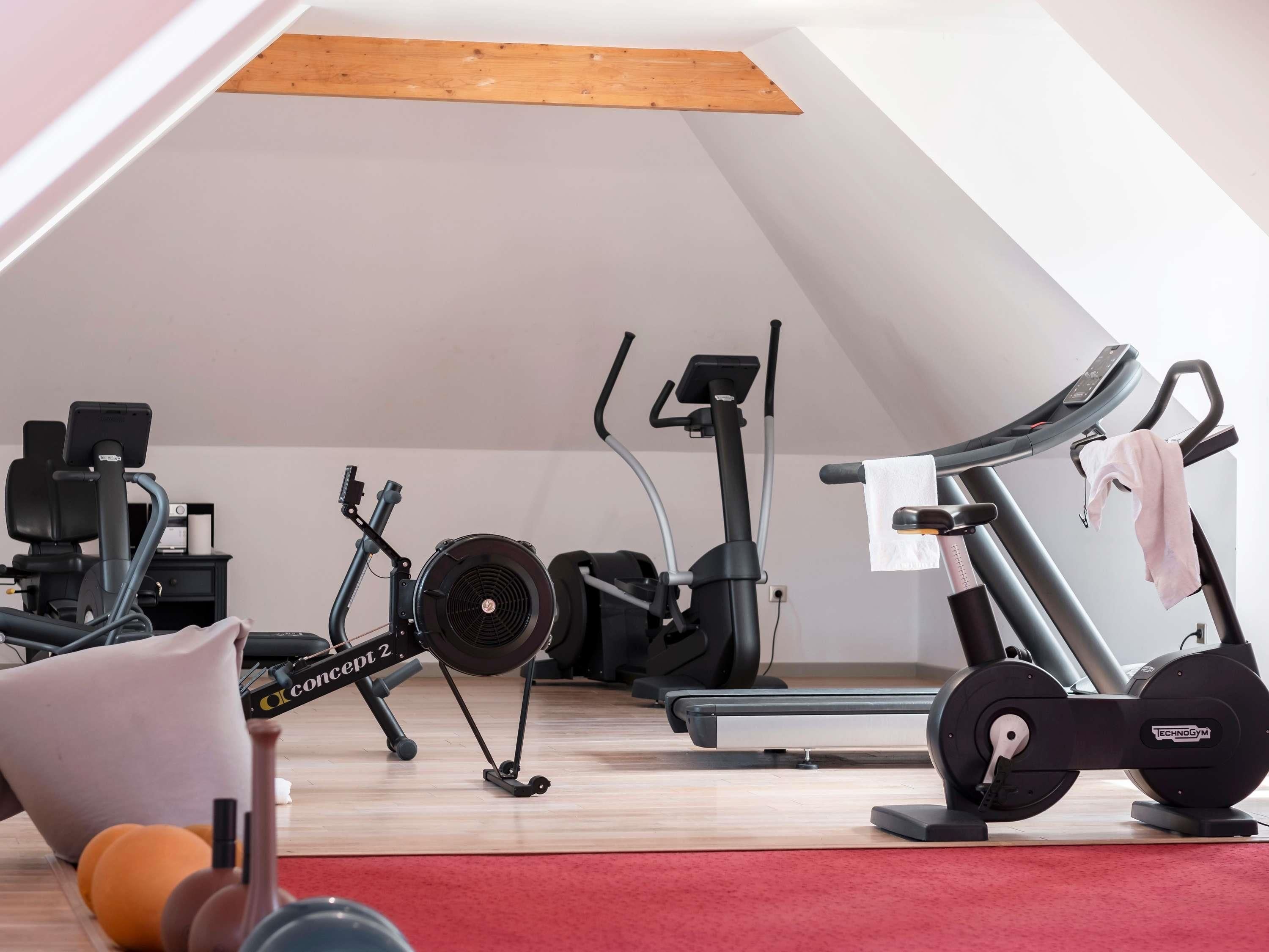 An attic room with a ceiling fan, exercise equipment, a treadmill, and a red carpet.