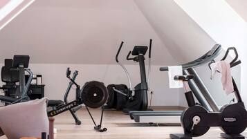 An attic room with a ceiling fan, exercise equipment, a treadmill, and a red carpet.