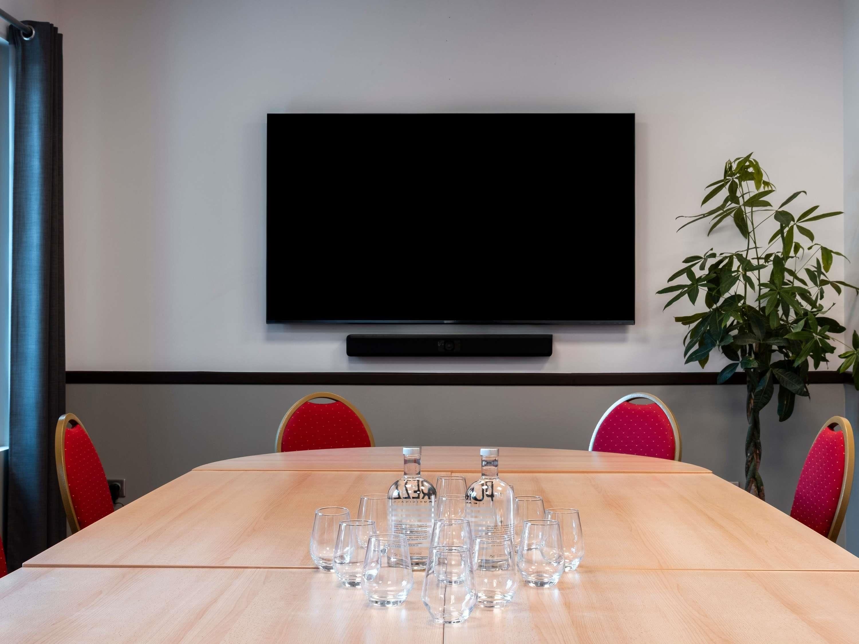 A conference room with a large table, chairs, a television, and a potted plant.