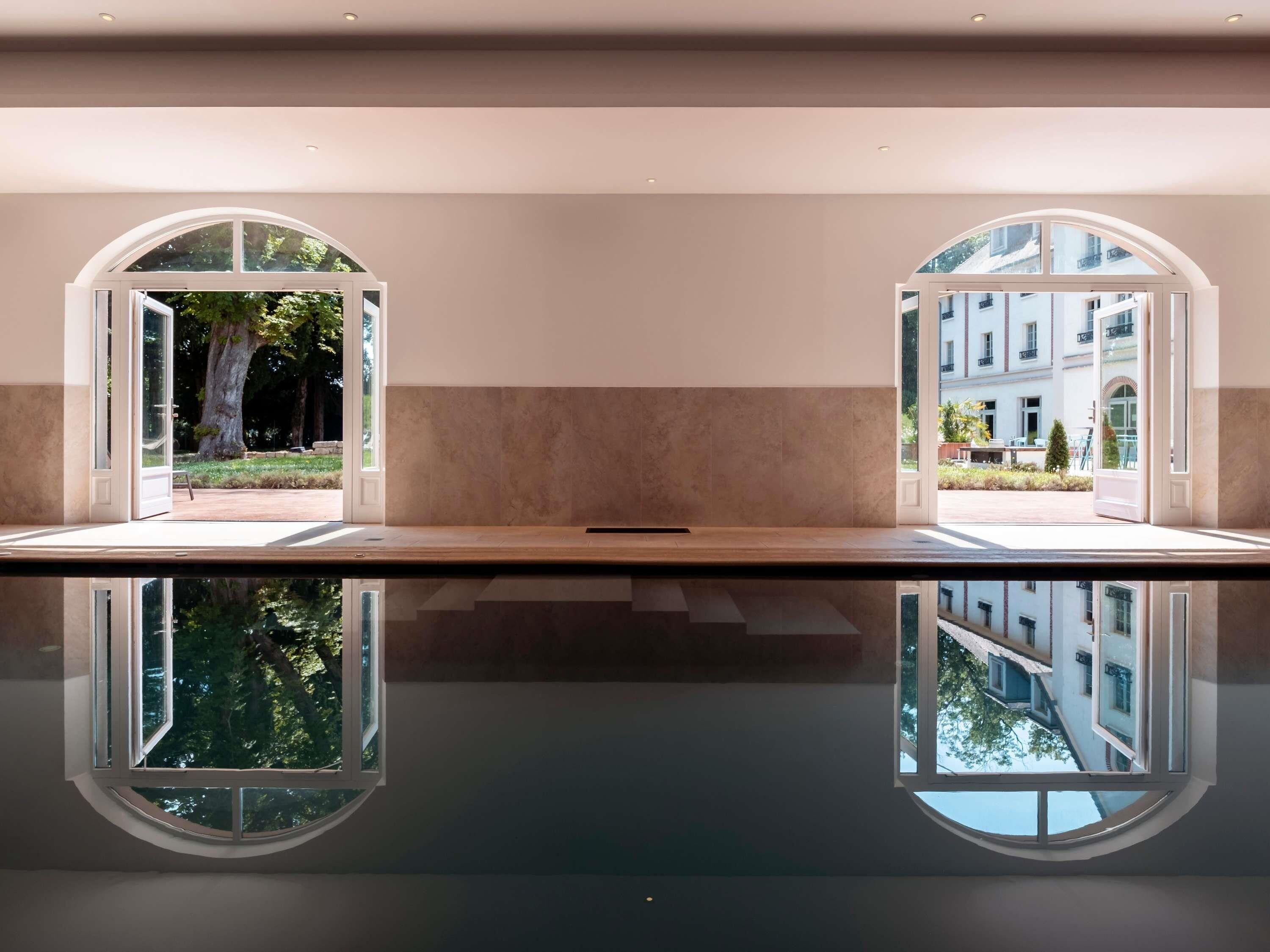 A hotel lobby with a reflective floor, two large arched windows, and a view of a building and greenery outside.