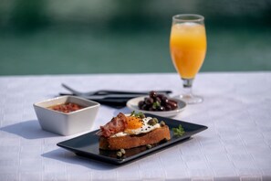 A breakfast setting with toast topped with eggs and bacon, a glass of orange juice, and small bowls of olives and tomato sauce.