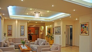 A spacious lobby with multiple seating areas, a reception desk, and a dining area. - Hotel Taxiarhis (Pineios)