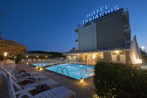 A hotel with a swimming pool, lounge chairs, and a well-lit outdoor area at dusk.