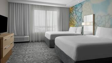 A hotel room with two beds, a TV, a dresser, and a large window with curtains.