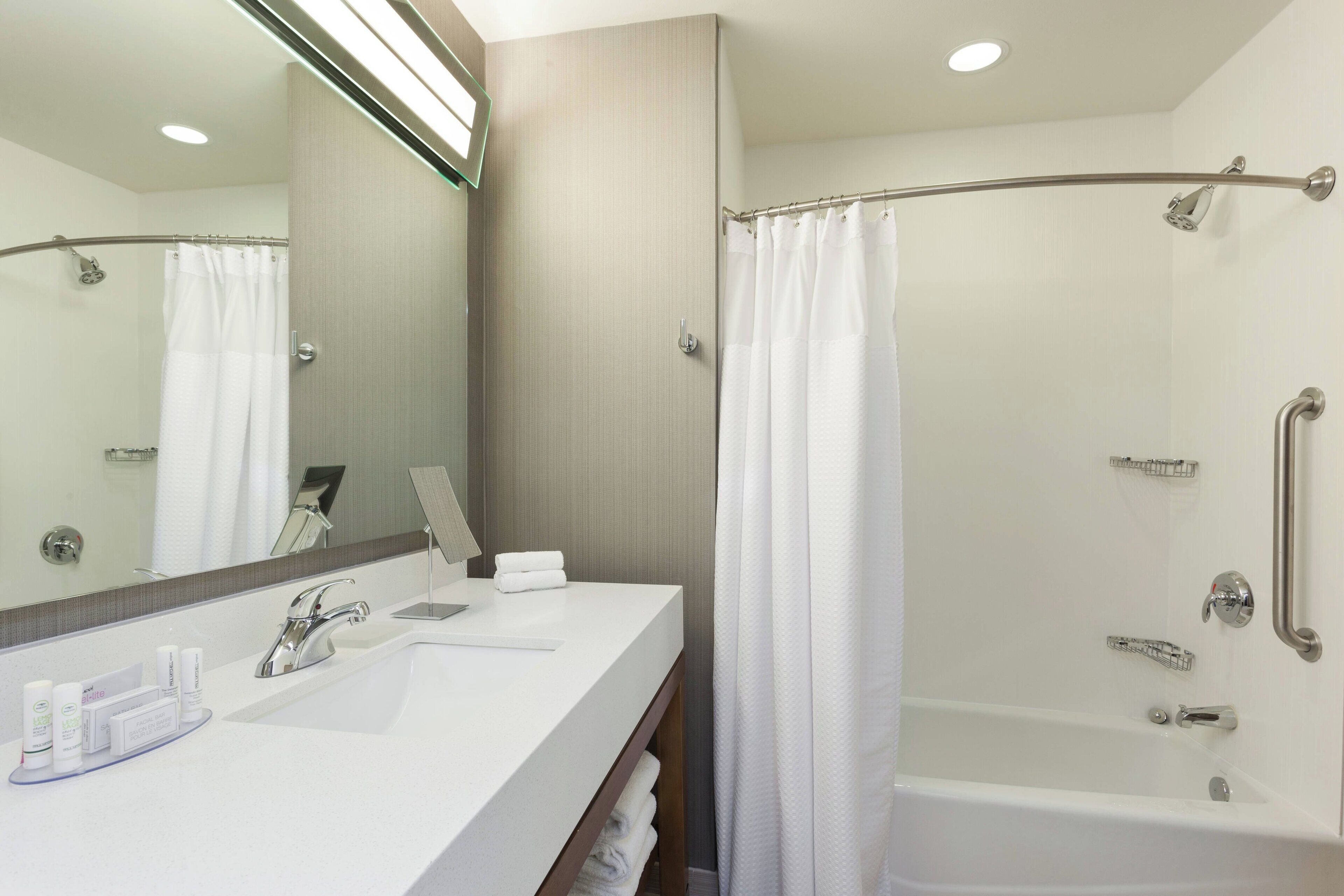 Un baño moderno con lavamanos, espejo y ducha blancos.