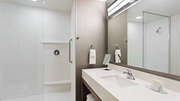 Un baño moderno con ducha envuelta en vidrio, un espejo grande y un tocador con lavabo y toallero.