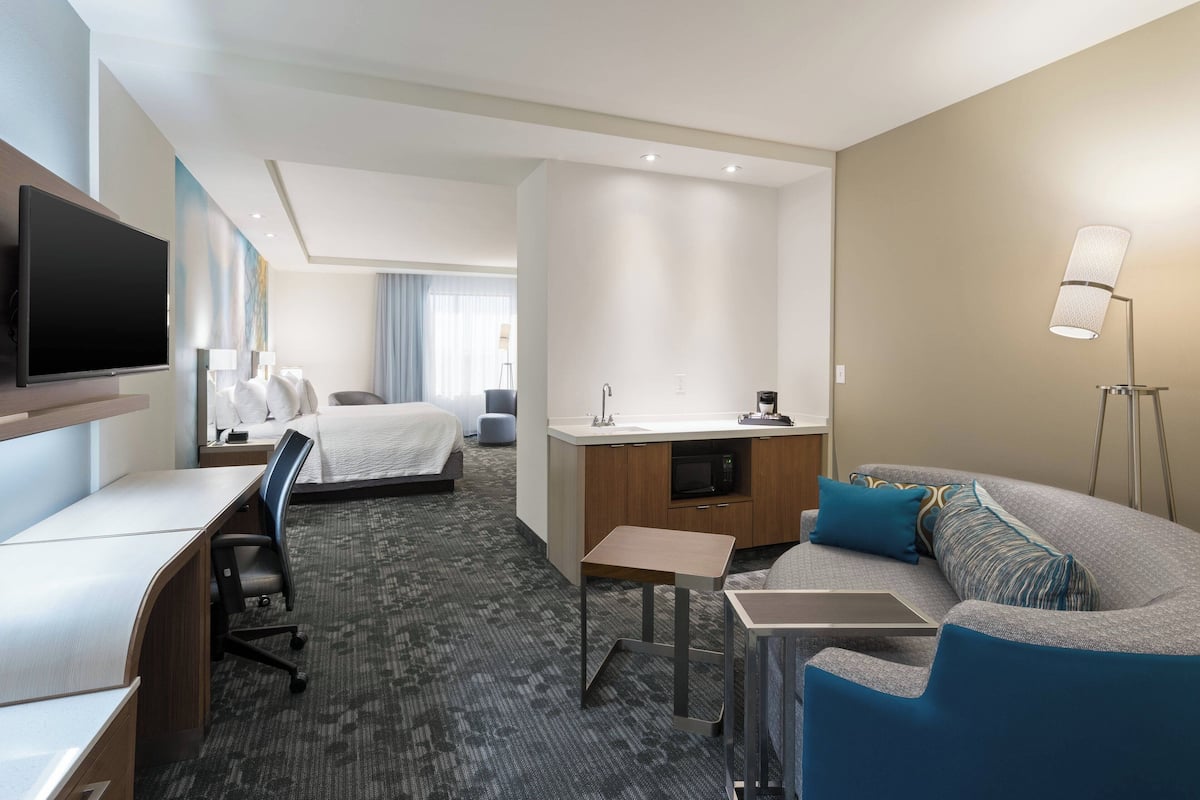 A hotel room with a bed, desk, chair, sofa, and a TV.