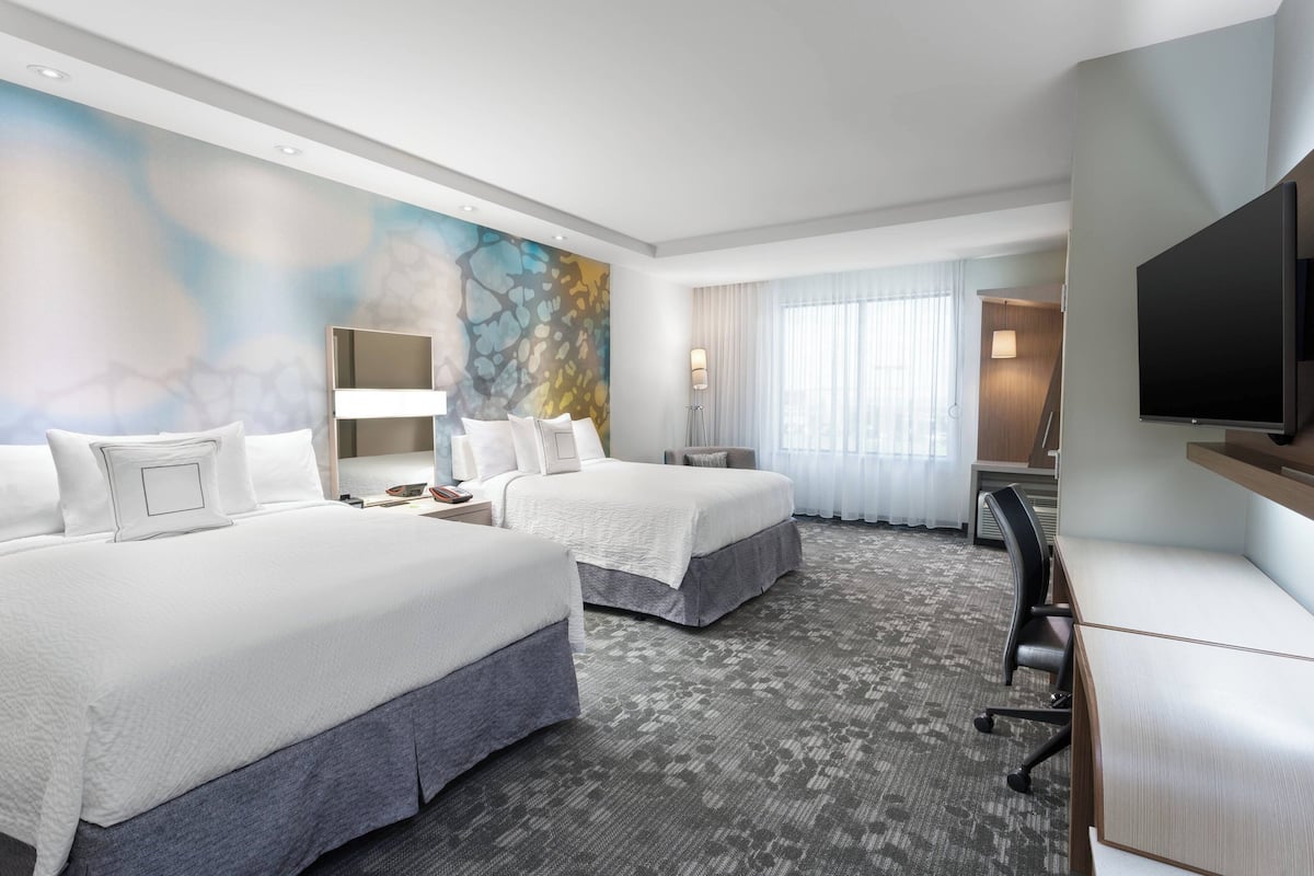 A hotel room with two beds, a desk, a TV, and a large abstract painting on the wall.