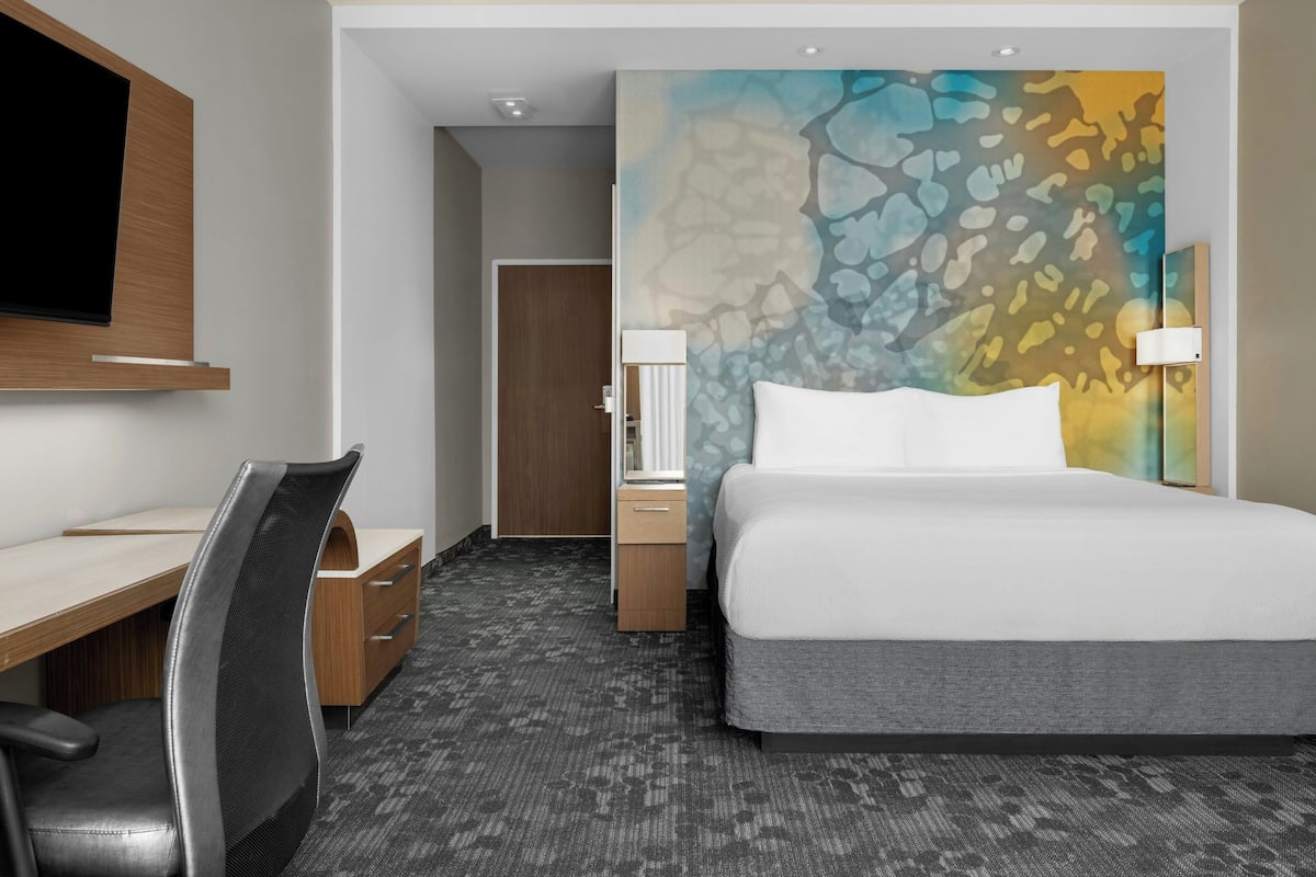 A hotel room with a bed, desk, chair, and a TV mounted on the wall.