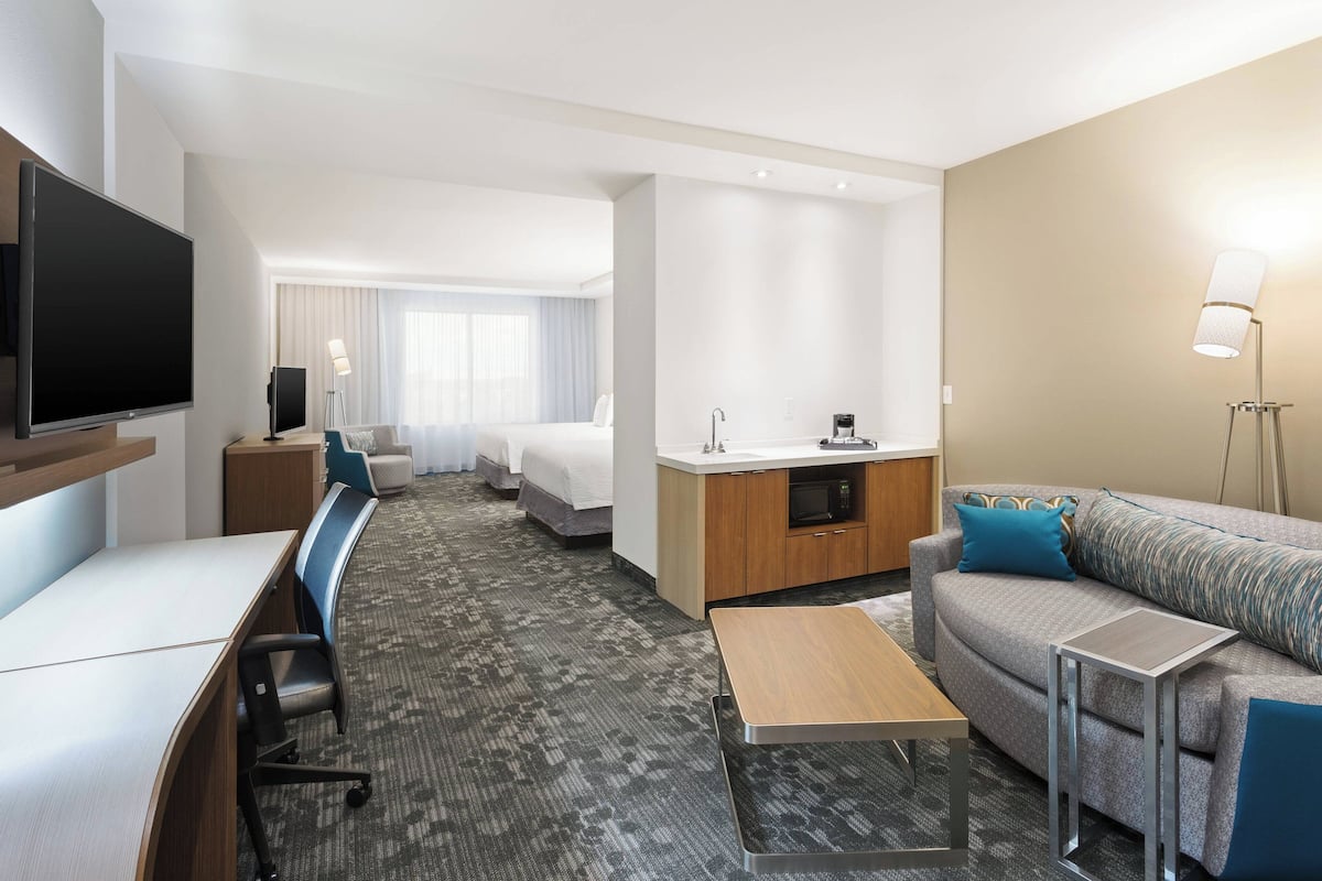 A hotel room with a flat-screen TV, a sofa, a coffee table, a desk, a kitchenette, and a bed.