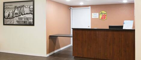 A reception area with a wooden reception desk, a framed welcome sign, and a Super 8 sign on the wall.