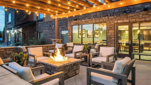 An outdoor patio with stone walls, wooden furniture, and a fire feature. - TownePlace Suites Billings (Billings)
