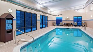 An indoor swimming pool with a tiled deck, a towel rack, and a seating area with tables and chairs. - TownePlace Suites Billings (Billings)