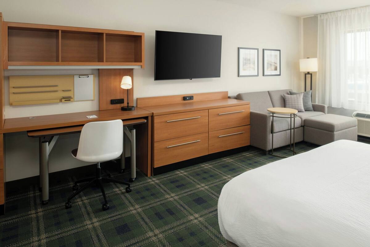 Habitación de hotel con cama, escritorio con silla, sofá, televisor y una pequeña mesa.