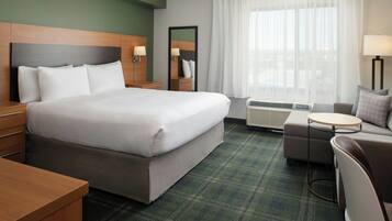A hotel room with a large bed, a small round table, a sofa, a mirror, and a window with curtains.
