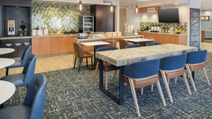 A modern hotel dining area with a central island, bar, and seating for guests. - TownePlace Suites Billings (Billings)