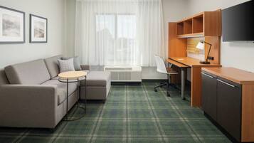Een moderne hotelkamer met een bank, een klein rond tafeltje, een bureau met stoel, een televisie en een kitchenette.