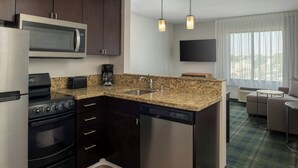 A compact kitchen with a microwave, stove, and dishwasher, a sink, and a flat-screen TV above the counter. - TownePlace Suites Billings (Billings)