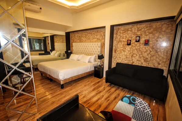 A hotel room with a large bed, a sofa, a wooden floor, and a patterned wall. - Cedros Inn Boutique Hotel (Guayaquil)