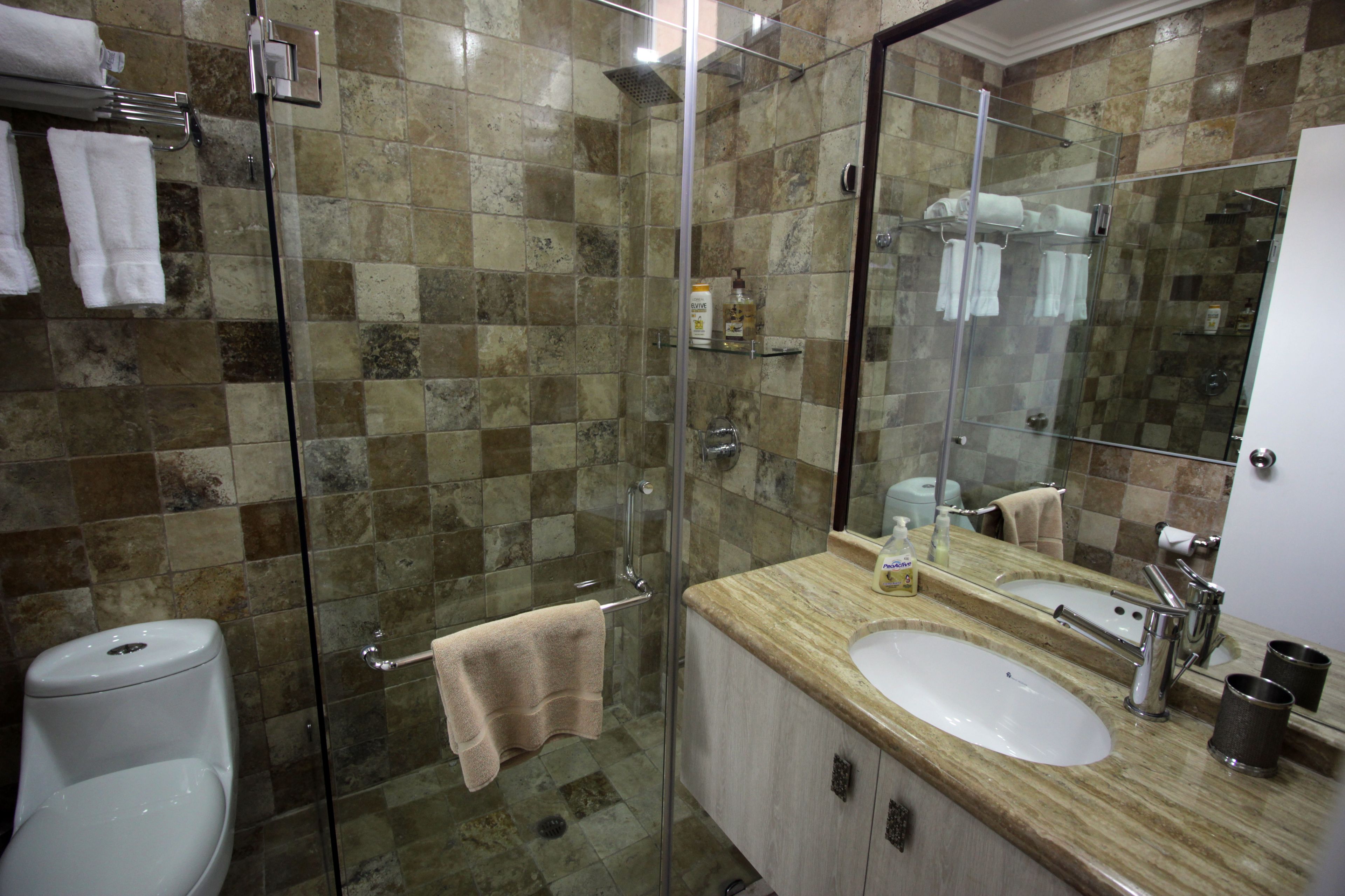 A bathroom with a glass shower enclosure, a white toilet, a sink with a mirror, and a towel rack.