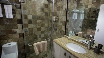 A bathroom with a glass shower enclosure, a white toilet, a sink with a mirror, and a towel rack.
