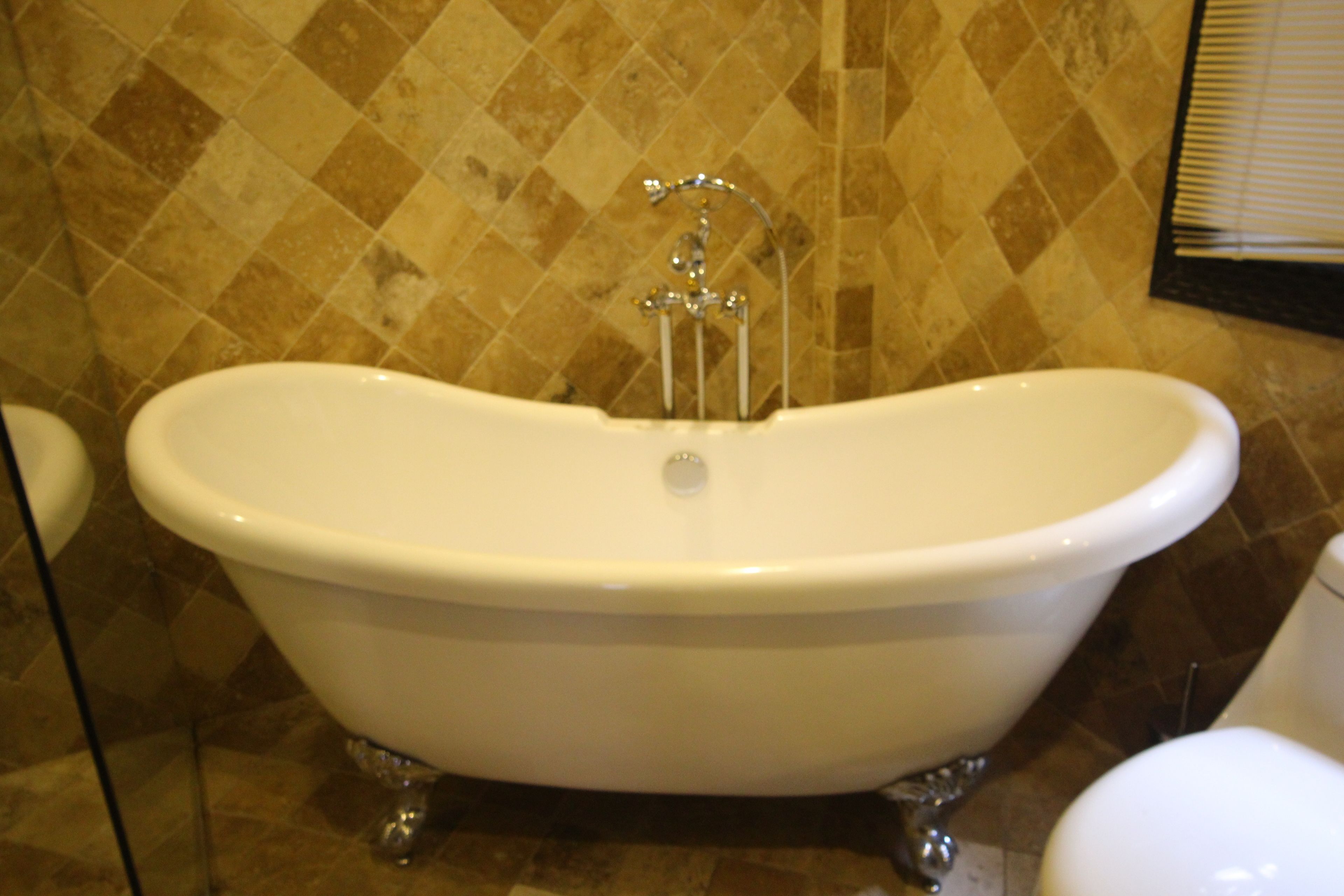 A white clawfoot bathtub in a bathroom with a tiled wall.