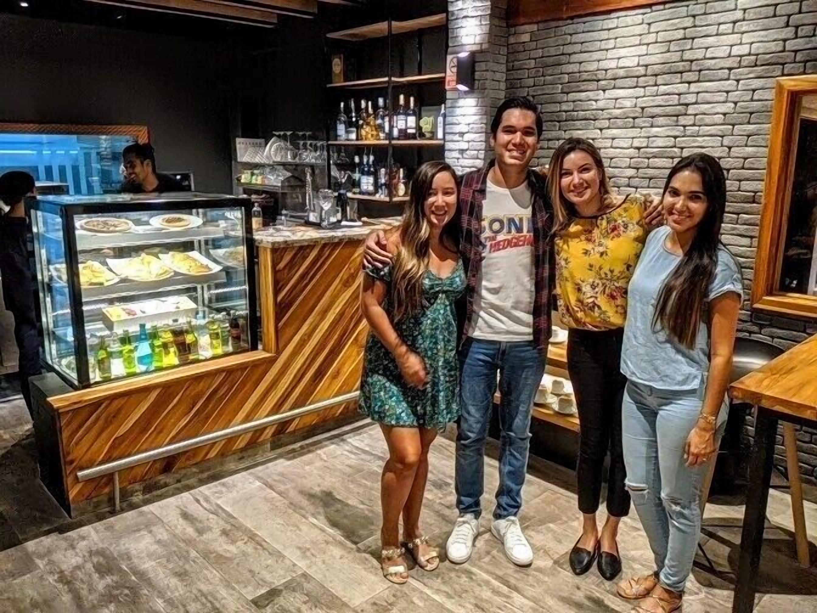 A group of people posing in a restaurant with a brick wall and a dessert display.