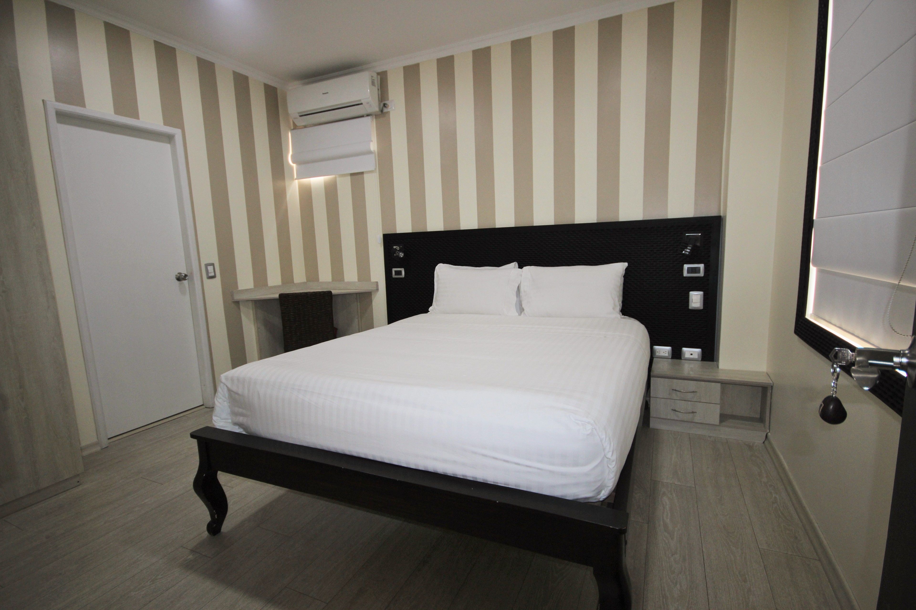 A neatly arranged bedroom with a large bed, a bedside table, a wardrobe, and a wall-mounted air conditioning unit.