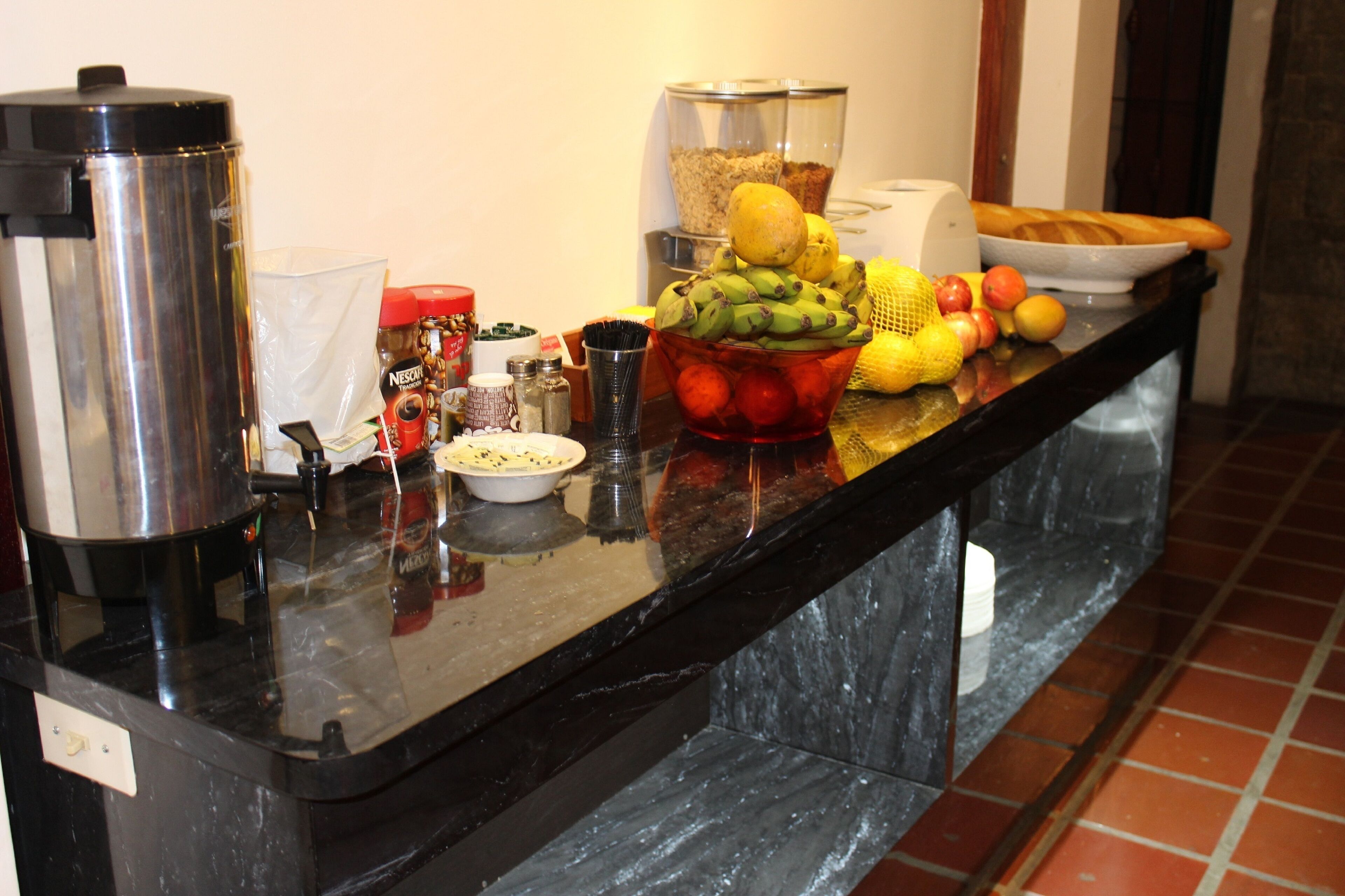 Una encimera de cocina con una cafetera, un cuenco de fruta y diferentes condimentos.