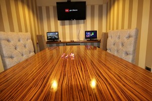 Una sala de conferencias con una gran mesa de madera, dos monitores y un televisor montado en la pared.