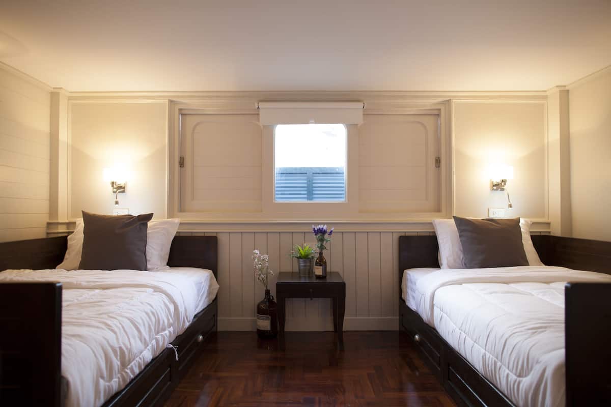 Habitación doble con dos camas, una mesita con un jarrón y una ventana con persianas.