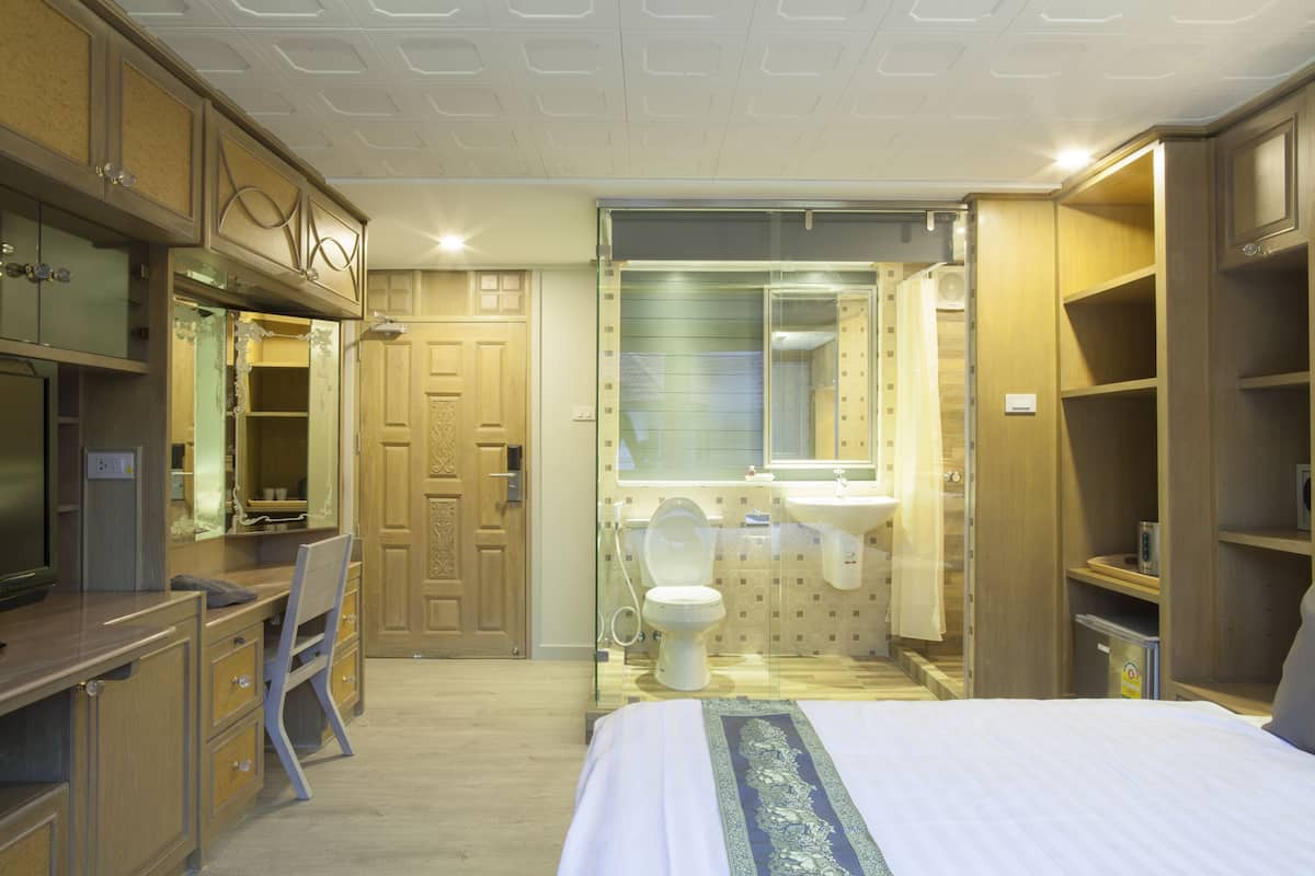 Una habitación de hotel con cama, escritorio, silla y baño completo con inodoro, lavabo y espejo.